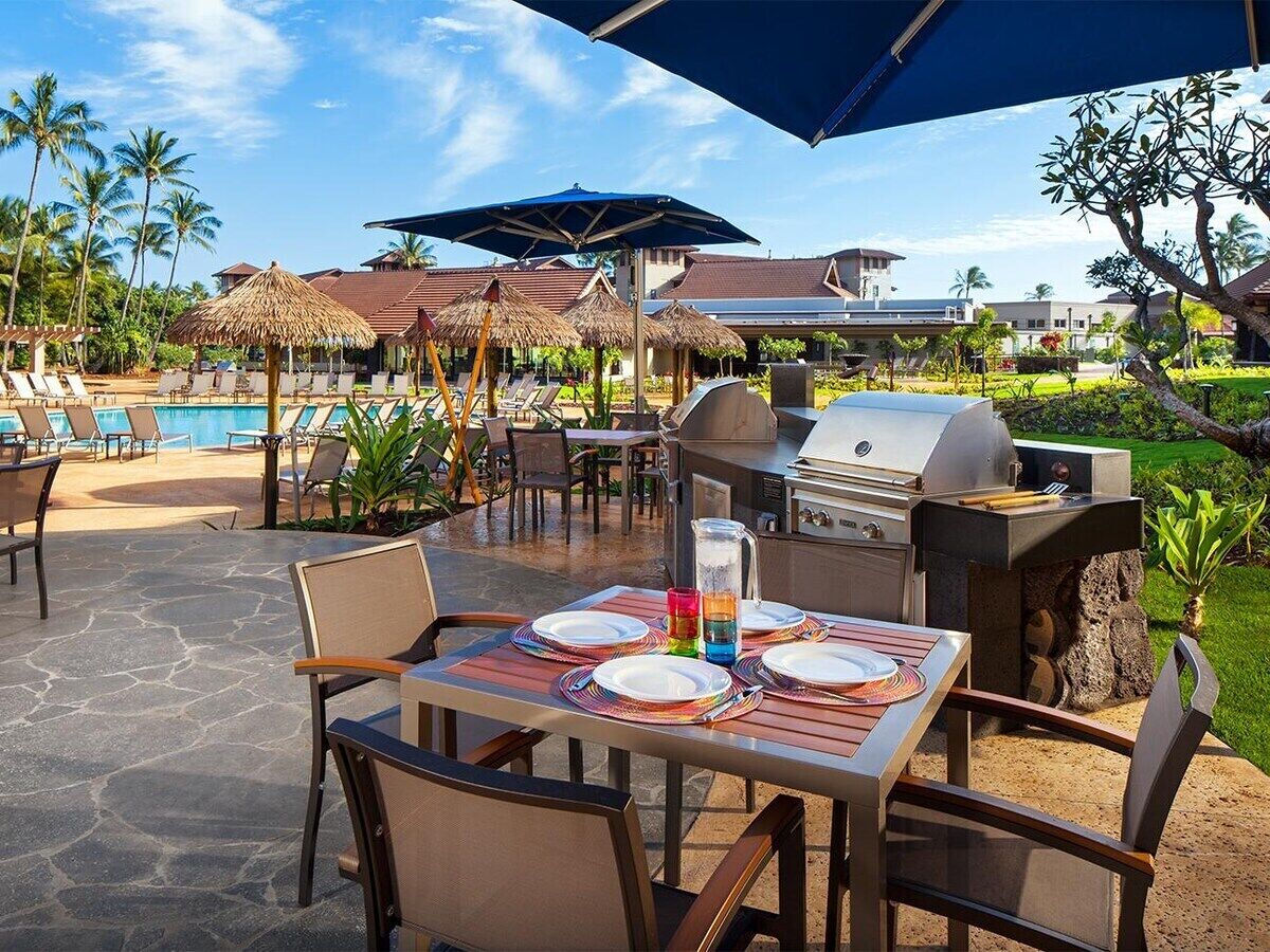 Ein Essbereich im Freien mit Grill, Liegestühlen und einem Pool im Hintergrund.