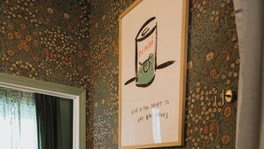 Un baño con papel tapiz floral, una cita enmarcada en la pared y una toalla colgada en un perchero de latón.