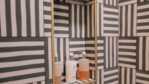 Un baño con paredes de baldosas a rayas y un espejo con repisa para artículos de tocador.