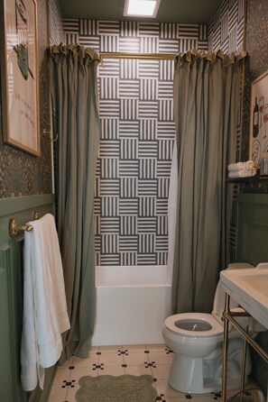 A bathroom with a patterned shower curtain, a toilet, and a sink with a towel rack.