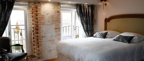 A bedroom with a large bed, a chair, a brick wall, and a window.