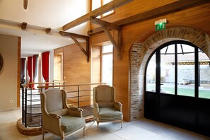 Quarto com duas poltronas estofadas, teto de madeira e uma grande janela em arco.