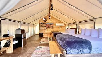 A tented accommodation with a bed, seating area, and kitchenette.