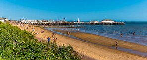 Ein Strand mit einem Steg, blauem Himmel und Menschen, die das Wasser genießen.