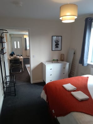Habitación de hotel con cama, escritorio y silla. Se ve una ventana con cortinas, una lámpara y un cuadro en la pared.