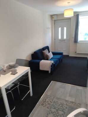 Ein Zimmer mit einem blauen Sofa, einem weißen Tisch mit einem Glas und einem gemusterten Teppich.