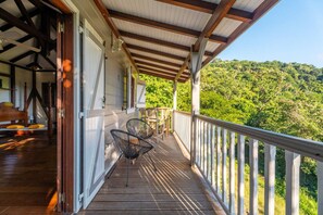 Une terrasse en bois avec une rambarde, un lit avec une tête de lit et une vue sur une colline boisée.