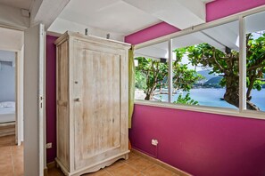 Huoneessa on suuri vaatekaappi, ikkunasta avautuu näkymä vehreään maisemaan ja vesistöön, ja lattia on laatoitettu.