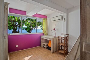 Ein Zimmer mit Fensterblick auf Baum und Wasser, ein Schreibtisch mit Lampe sowie ein Stuhl.