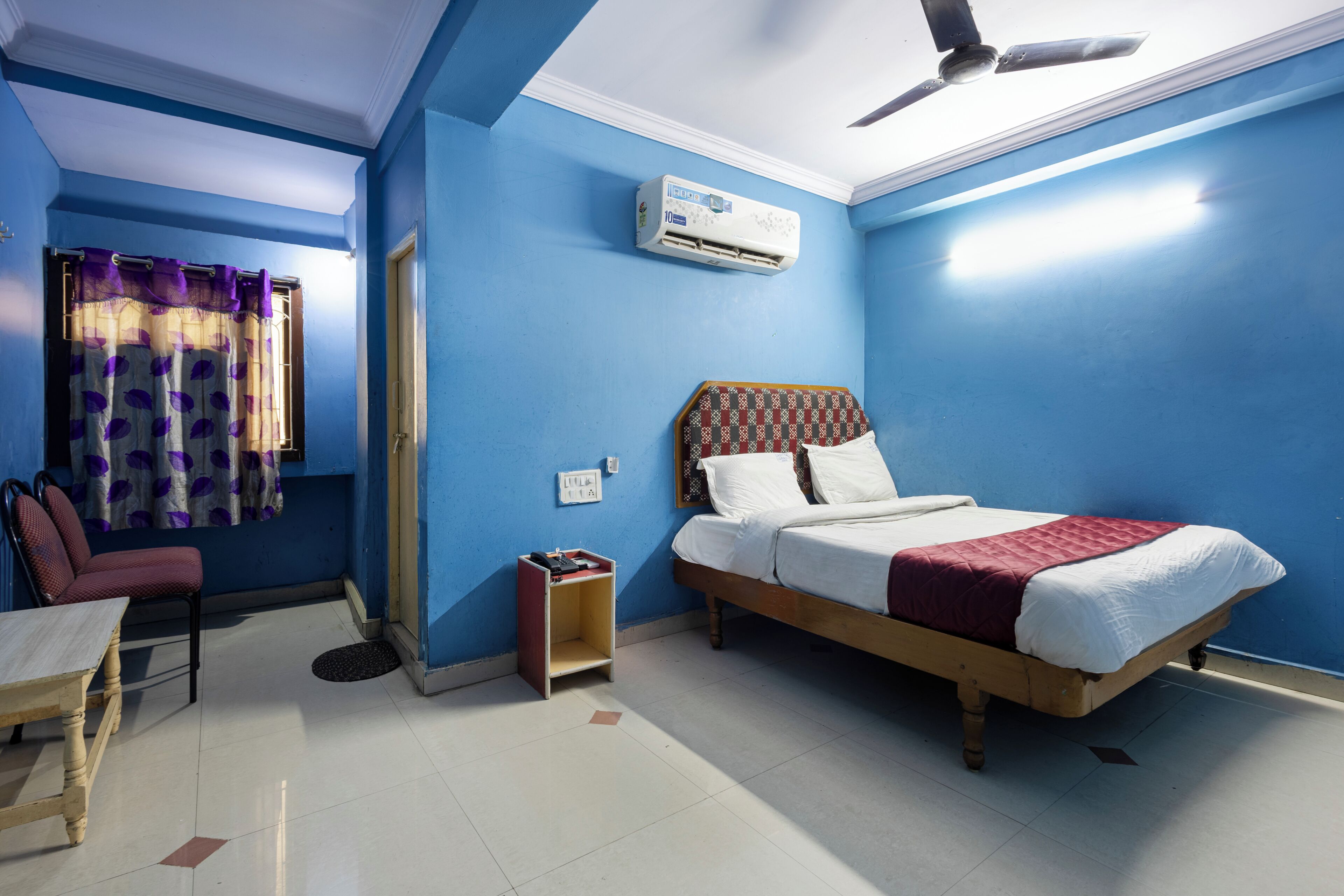 A room with a bed, a chair, an air conditioning unit, and a ceiling fan.
