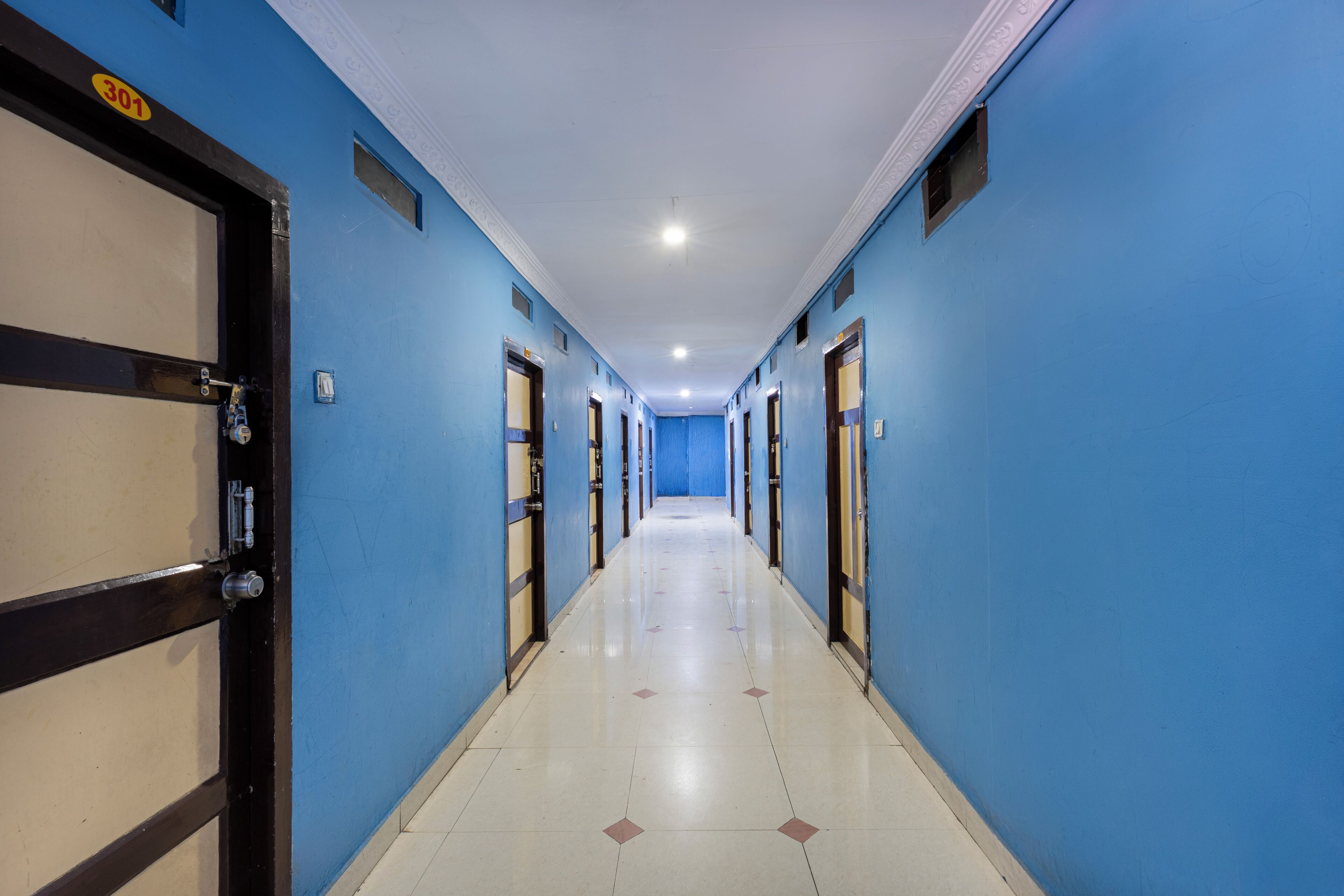 A hotel corridor with blue walls, doors with numbers, and a tiled floor.
