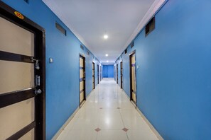 A hotel corridor with blue walls, doors with numbers, and a tiled floor.