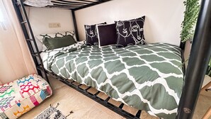A bunk bed with a patterned bedspread, pillows with abstract designs, a small rug, and a potted plant. - Stylish 2BR Apartment Near Harhoura Beach- PS5, Free Parking & Fast Wi-Fi (Temara)