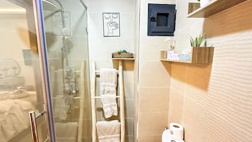 Une salle de bain avec une douche à parois de verre, une échelle en bois sur laquelle sont posées des serviettes, des toilettes et une étagère contenant des articles de toilette.