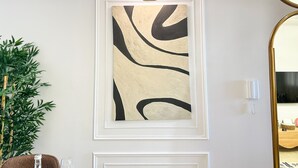 A framed abstract painting on a wall, a potted plant, and a mirror with a gold frame. - Stylish 2BR Apartment Near Harhoura Beach- PS5, Free Parking & Fast Wi-Fi (Temara)
