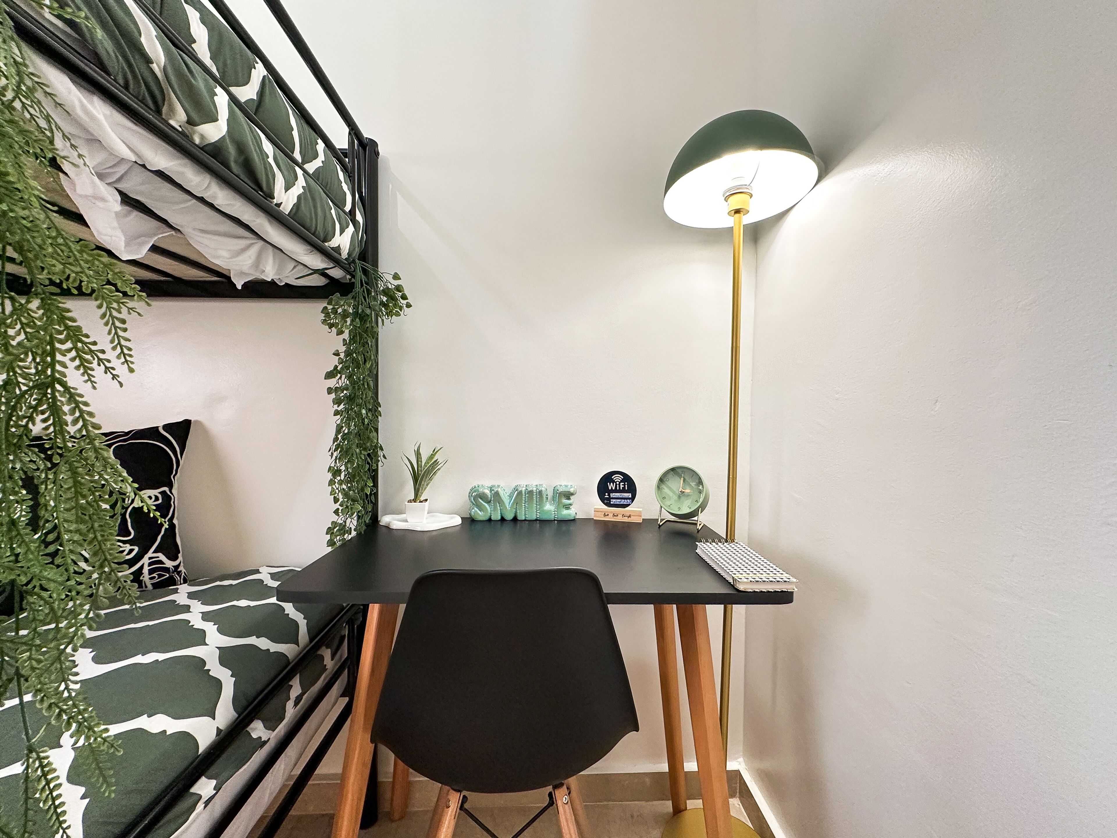 A compact room with a bunk bed, a desk with a lamp, a chair, and a small potted plant.