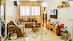 A modern living room with a sofa, coffee table, and entertainment unit. - Stylish 2BR Apartment Near Harhoura Beach- PS5, Free Parking & Fast Wi-Fi (Temara)