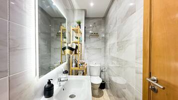 Une salle de bain moderne avec un grand miroir, un lavabo blanc, des toilettes et un espace douche.