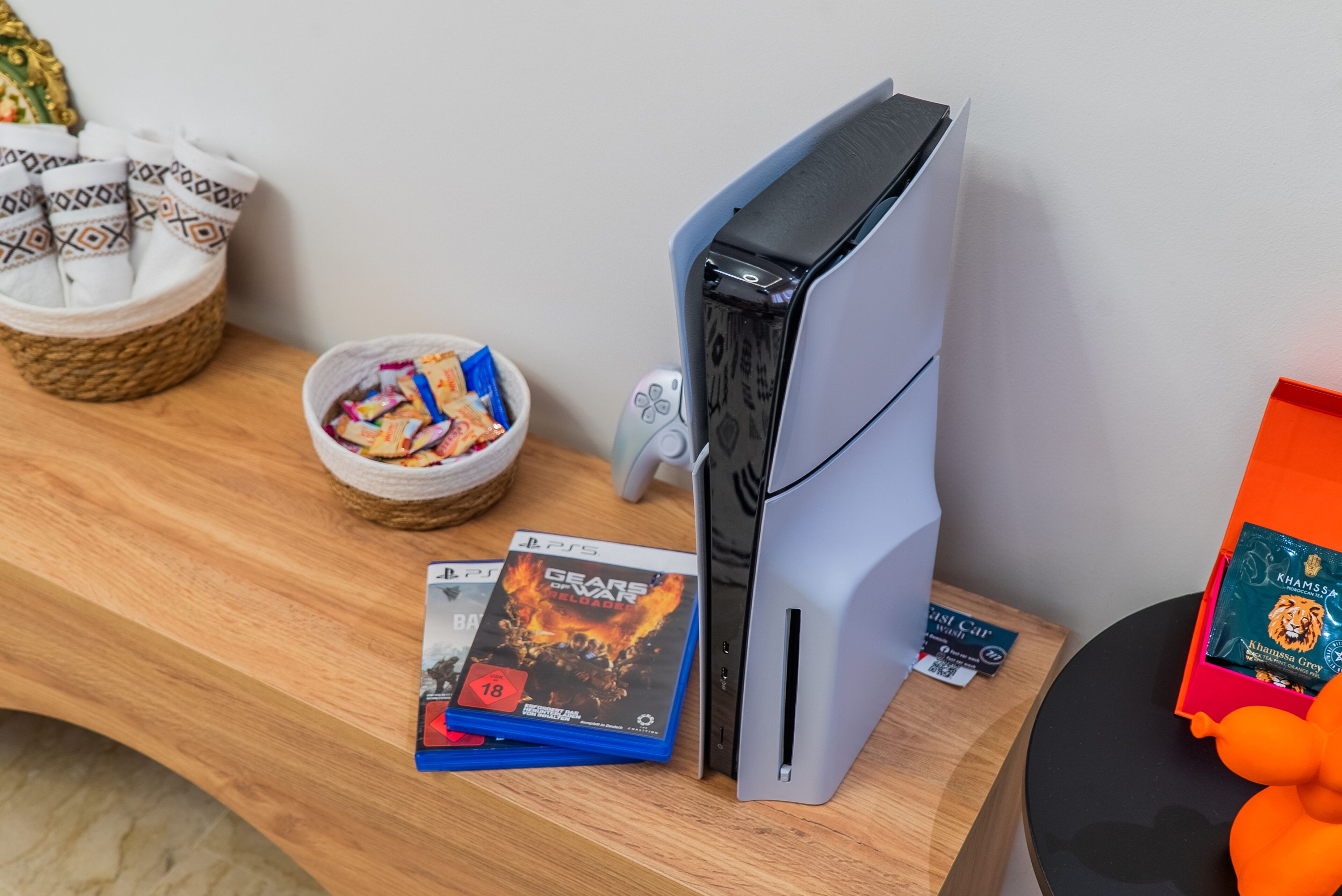 Une console PlayStation 5 posée sur une table en bois, avec un bol de collations et une manette de jeu.