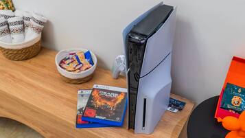 Une console PlayStation 5 posée sur une table en bois, avec un bol de collations et une manette de jeu.