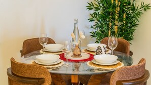 A round dining table with white plates, glasses, and a bottle, surrounded by brown upholstered chairs. - Stylish 2BR Apartment Near Harhoura Beach- PS5, Free Parking & Fast Wi-Fi (Temara)