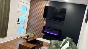 Un soggiorno moderno con un divano verde, un tavolino in legno, una TV a schermo piatto montata su una parete nera e una finestra con tende.