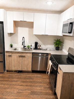 Una cucina moderna con mobili bianchi, una lavastoviglie in acciaio inossidabile, un piano cottura nero e un forno a microonde.