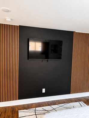 A room with a black wall, a mounted flat-screen TV, and wooden paneling on the sides. - Cozy 1BR - Sleeps 4 - Walk to Downtown & Free Parking (Dallas)