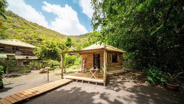 Eine rustikale Holzhütte mit Veranda, umgeben von üppigem Grün und einer Bergkulisse.