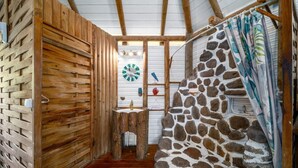 Ein rustikales Badezimmer mit Holzwänden, einer Wand aus Stein und einer Dusche. Es enthält ein Waschbecken mit Spiegel.