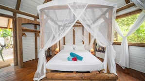 Ein Zimmer mit einem Bett unter einem Baldachin, Holzbalken und Blick ins Grüne.