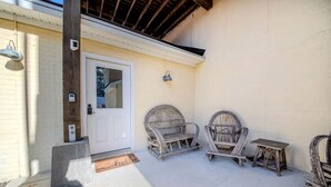 A covered patio with two wicker chairs and a small table, a white door, and a light fixture on the wall. - Waterfront River Cottage with Pool Dock Kayaks and Game Room in Hartfield Virginia (Topping)