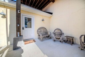 A covered patio with two wicker chairs and a small table, a white door, and a light fixture on the wall. - Waterfront River Cottage with Pool Dock Kayaks and Game Room in Hartfield Virginia (Topping)