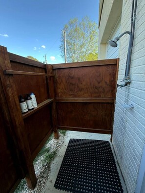 A wooden outdoor enclosure with a metal grate at the entrance, a white wall with a window, and a metal pipe on the wall. - Waterfront River Cottage with Pool Dock Kayaks and Game Room in Hartfield Virginia (Topping)