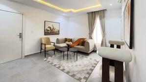 A modern living room with a sofa, armchairs, a coffee table, and a painting on the wall. - Premium 1-Bedroom in Victoria Island with Pool, Fast Wi-Fi & 24/7 Power (Lagos)