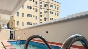 A swimming pool with a metal handrail, a tiled edge, and a building in the background. - Premium 1-Bedroom in Victoria Island with Pool, Fast Wi-Fi & 24/7 Power (Lagos)