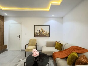 A modern living room with a sofa, a chair, a coffee table with a vase of flowers, and a painting on the wall. - Premium 1-Bedroom in Victoria Island with Pool, Fast Wi-Fi & 24/7 Power (Lagos)