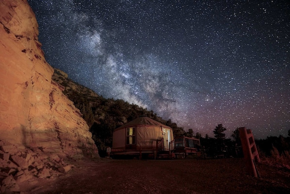 Una yurta con vista despejada de la Vía Láctea, con un risco rocoso de fondo.