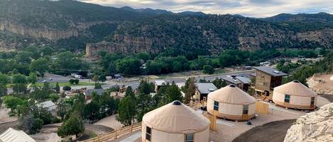 A yurt camp with multiple yurts, a dirt path, and a mountainous backdrop.