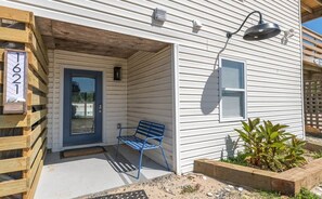 A residential property with a front porch, a blue bench, a wooden fence, and a number sign. - Blue Moon Outer Banks (Currituck County)