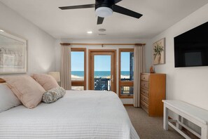 A bedroom with a bed, a ceiling fan, a dresser, and a view of the beach. - Salty Moon Outer Banks (Currituck County)
