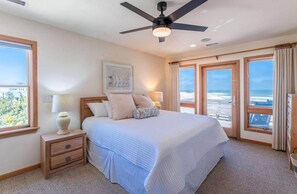 Un dormitorio con cama, mesita de noche, lámpara, ventilador de techo y ventanas amplias con vistas.