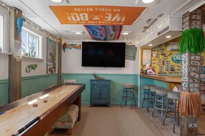 A room with a pool table, bar stools, a television, and various wall decorations. - Salty Moon Outer Banks (Currituck County)