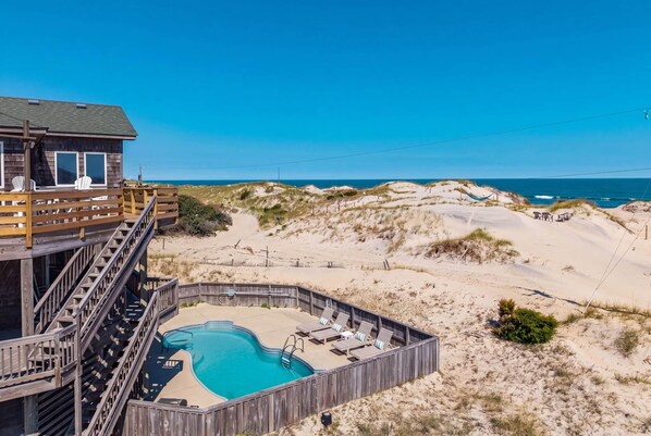 A beachfront property with a wooden deck, a swimming pool, and a view of the ocean. - Salty Moon Outer Banks (Currituck County)