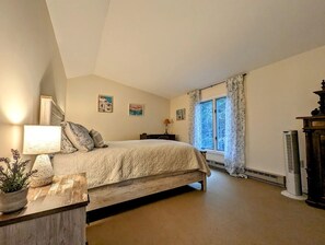 A bedroom with a bed, a bedside lamp, a window with curtains, and a radiator. - Idyllic Waterfront Cottage with Fire Pit Near Acadia National Park | Gouldsboro, Maine (Gouldsboro)