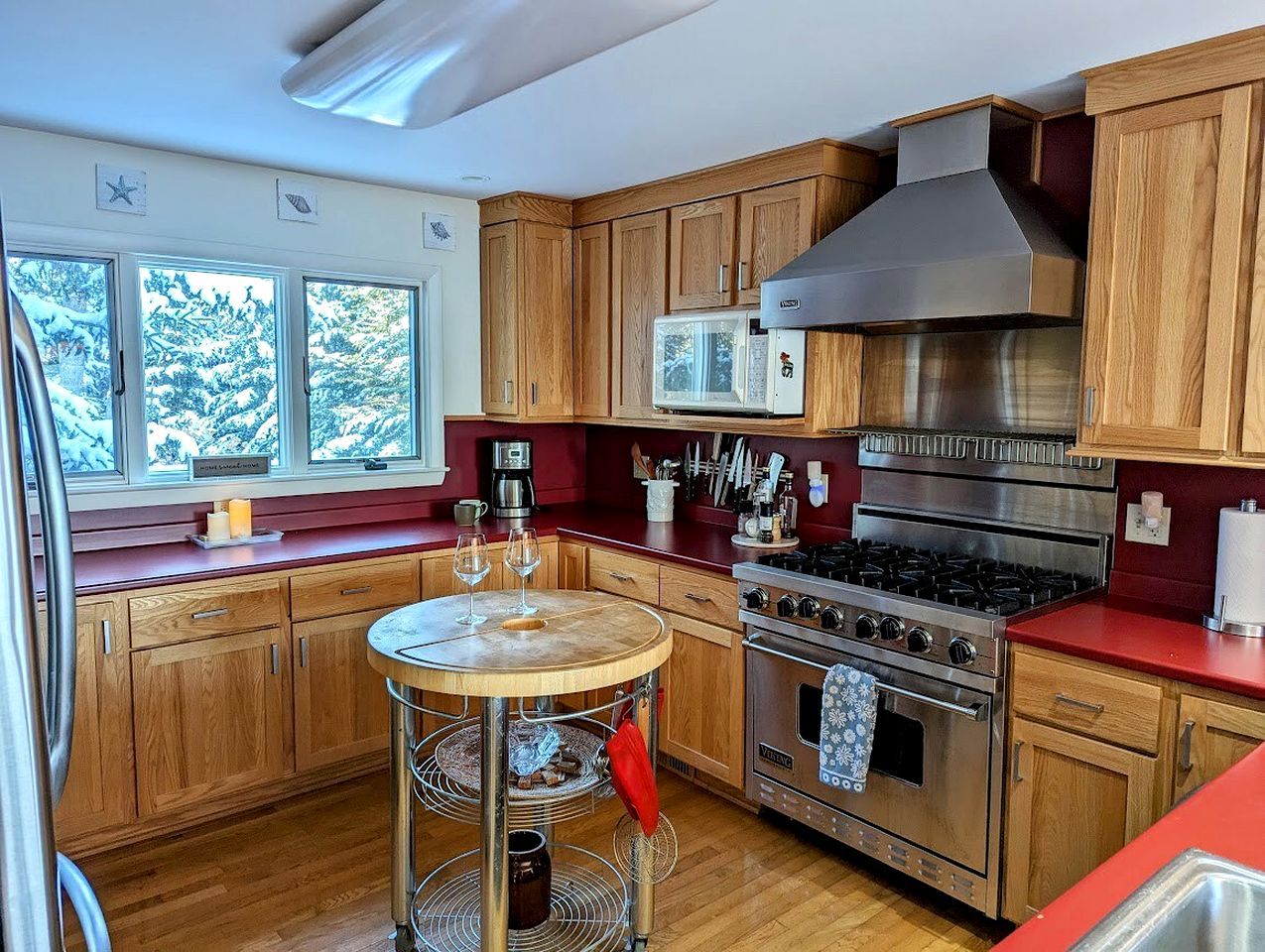 Una cocina con armarios de madera, una estufa de acero inoxidable y una mesa redonda con copas de vino.