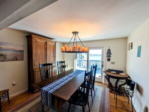 A dining area with a wooden table, chairs, a chandelier, and a view of the outdoors. - Idyllic Waterfront Cottage with Fire Pit Near Acadia National Park | Gouldsboro, Maine (Gouldsboro)
