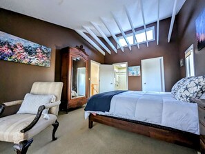 Um quarto com uma cama, uma cadeira, cômoda, espelho e um quadro na parede.