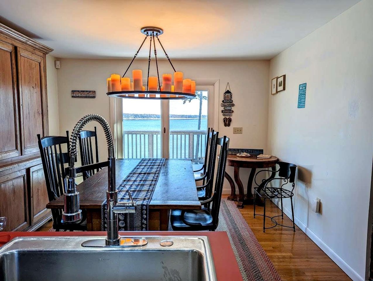A dining area with a large table, chairs, a chandelier, and a view through a glass door.