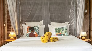 A bed with white linens, two pillows with tropical prints, a yellow towel, and two bedside lamps.